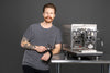 Zach poses next to his favorite espresso machine, the ECM Synchronika AMG Edition, portafilter in hand.