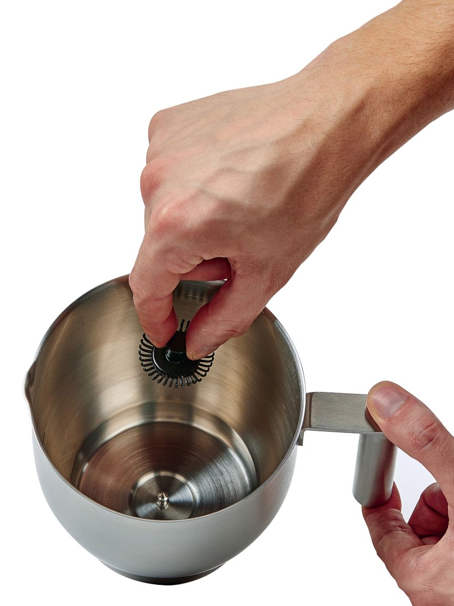 Top down view of frothing whisk being removed from milk carafe.
