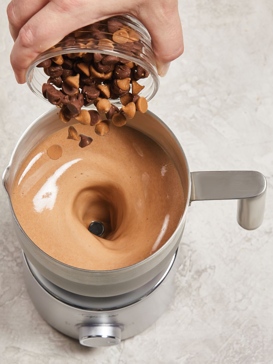 Top down view of butterscotch chips being added to the milk carafe.