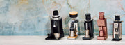 Line up of 5 grinders on a white counter top in front of a marble blue wall.