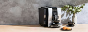 JURA Super-Automatic Espresso Machine on a wooden counter in front of a smokey gray wall.