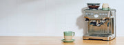 Breville Barista Express on a counter with green mugs and a saucer plate