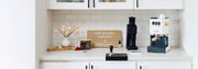 Gaggia Classic E24 in white next to a Varia VS4 and other coffee accessories in a white kitchen setting and coffee nook.