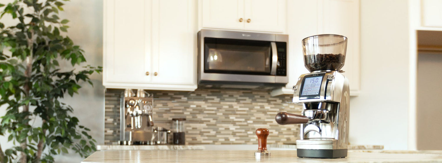 An all-purpose coffee and espresso grinder with a portafilter attached, with a modern kitchen backdrop.