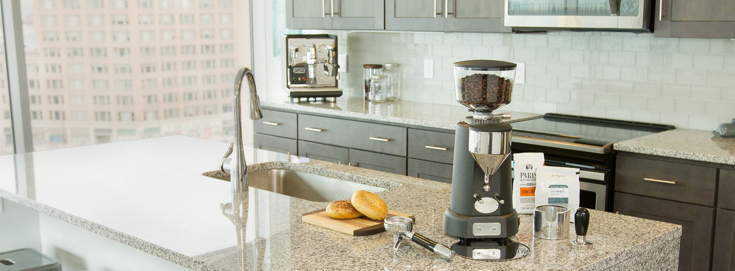 An espresso grinder on a granite counter next to a portafilter.