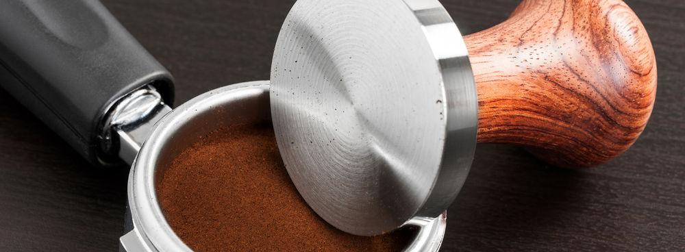 Coffee tamper leaning on a portafilter filled with ground coffee