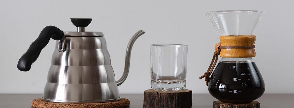 A goosneck kettle, coffee mug, and pour over coffee brewer sitting on wooden pedastals.