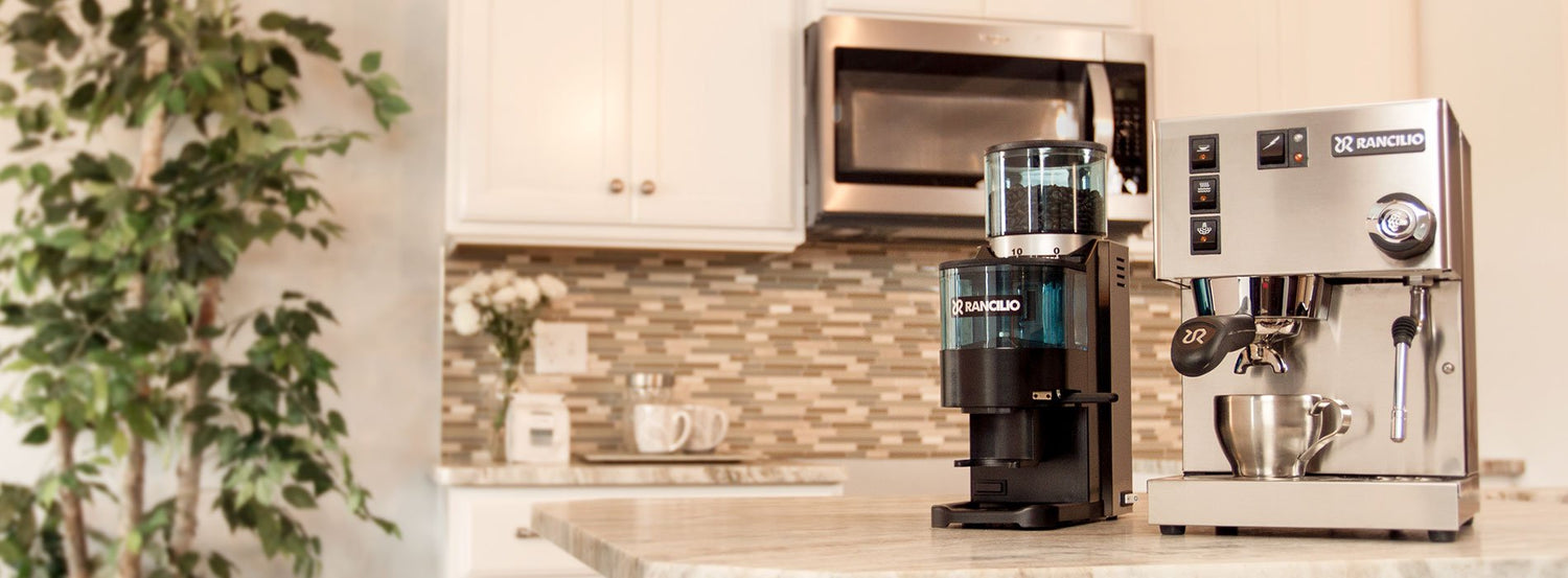 A Rancilio espresso machine and coffee grinder on a marble counter in an off-white kitchen