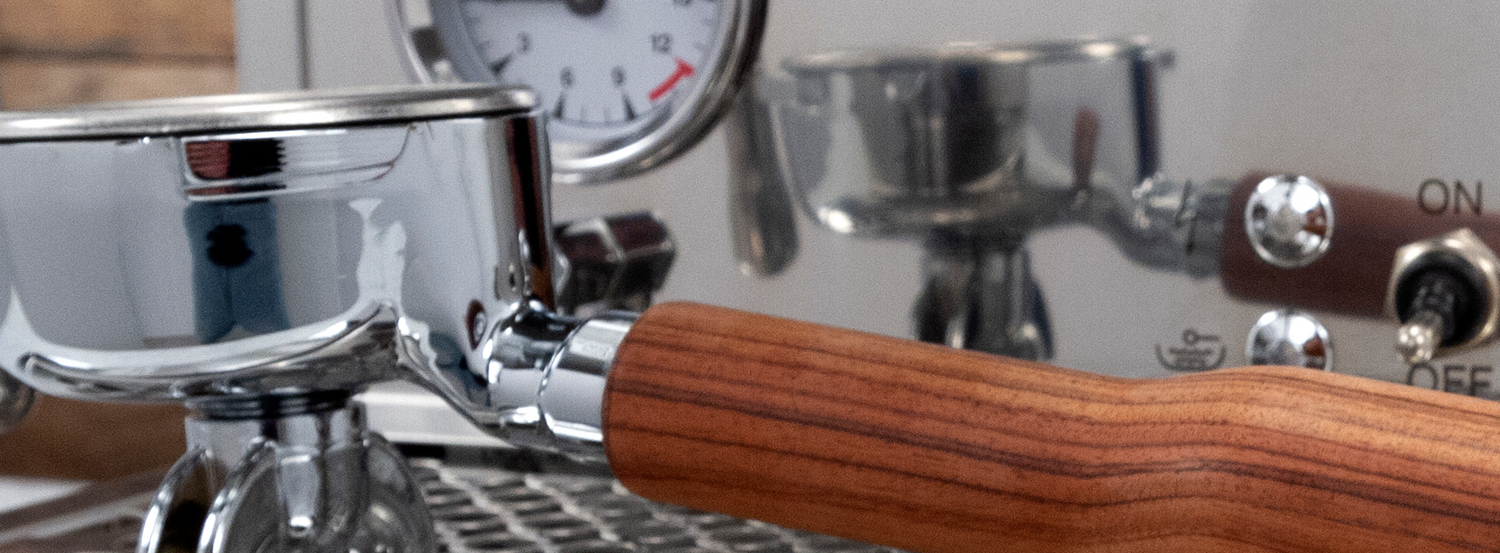 A portafilter with a wooden handle resting on the drip tray of a wood accent espresso machine.