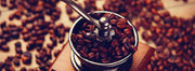 Coffee beans scattered around and inside of a manual coffee grinder