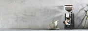 Eureka Mignon Silenzio 55 in Black with Walnut accents on a gray stone counter and gray background next to latte cups.