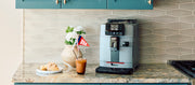 Close up of the Gaggia Cadorna Prestige in Moonlight Gray on a kitchen counter next to a pastry and iced coffee drink.
