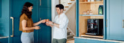 Man and Woman drinking coffee next to a Gaggia Accademia in blue kitchen.