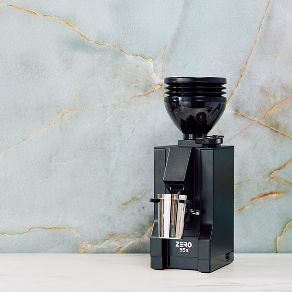 Eureka Mignon Zero 55s in black on a white counter top in front of a blue slate wall.