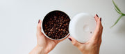Close-up of a person opening a coffee Fellow Atmos in white with coffee beans in it.