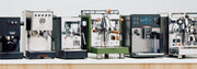 Row of various espresso machines on a white background.