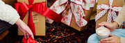Close-up of hands with coffee and wrapped gifts on a patterned surface.