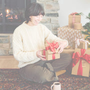 Woman opening gifts from Whole Latte Love with a cup of coffee sitting in front of a fire.
