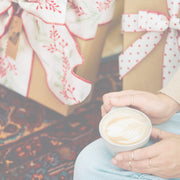 Close-up of a person holding a cup of coffee sitting on a rug with gifts in the background.