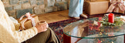 Person sitting on a couch holding a cup with a gift next to them, in a cozy living room setting.