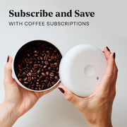 Person opening a Coffee Fellow Atmos in white with coffee beans and promotional text that reads "Subscribe and Save with coffee subscriptions".
