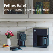 Fellow Aiden and the Fellow Ode Brew Grinder on a counter next to a scale with promotional text that reads "Fellow Sale, Save on Premium Brewing Equipment".