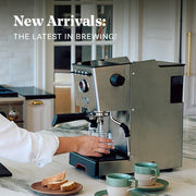 Person using a Gaggia Classic GT with text 'New Arrivals: The Latest in Brewing' in a kitchen setting.