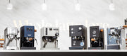 Close-up of a line up of 6 best of espresso machines of 2026 on a white and black counter in front of a white wall with lights hanging above.