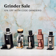 Four countertop coffee grinding devices displayed side by side on a white surface against a light blue marble-patterned background, with promotional text at the top reading 'Grinder Sale 10% OFF WITH CODE GRINDER10'. The products include black, silver, gold, and rose gold color options.
