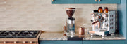 Rocket Appartamento and Rocket Grinder on a marble kitchen counter next to a stove and other espresso brewing accessories.