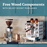 Rocket Appartamento and Rocket Grinder on a marble kitchen counter next to a stove and other espresso brewing accessories. Promotional text ovlerayed that reads "Free Wood Components - With select rocket purchases".