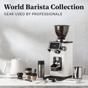 Close-up of a Ceado REV Zero grinder in white next to a varia smart kettle, notNeutral pico cups, a revolution milk frothing pitcher, spoons, scale and tampers on a white counter top in front of a white tiled wall. Promotional text overlayed that reads "World Barista Collection - Gear used by professionals".