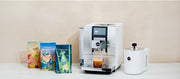 Close-up of a JURA Z10 in White next to a white JURA Cool Control and Whole Latte Love coffee bags on a white counter in front of a beige wall.