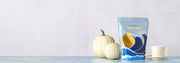 Whole Latte Love Crema Wave on a blue counter next to a coffee mug and white pumpkins in front of a white tiled wall. 