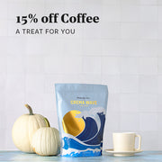Whole Latte Love Crema Wave on a blue counter next to a coffee mug and white pumpkins in front of a white tiled wall. Promotional text overlayed that reads "15% Off coffee - A treat for you".