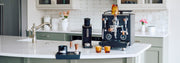 Profitec DRIVE Espresso Machine in black with wooden accents next to espresso accessories on a kitchen counter. 