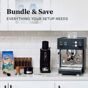 Close-up of the Profitec MOVE in black on a white coffee counter next to a Profitec Twist SD54 in black and other coffee accessories. Promotional text overlayed that reads "Bundle & Save - Everything Your Setup Needs".