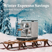 Profitec JUMP on a wooden sled in front of a winter forest with snow falling. Promotional text that reads "Winter Espresso Savings - Hot and Ready Apres-so".