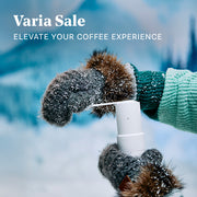 Person in mittens using a Varia EVO Hand Grinder in white in a winter setting. Promotional text overlayed that reads "Varia Sale".