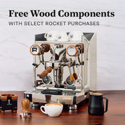 Rocket Espresso Giotto V Fast with Olive Wood Accents with other wooden accents in front of it on a wooden counter top. Promotional text that reads "Free Wood Components - With Select Rocket Purchases".
