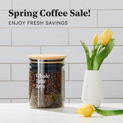 Whole Latte Love coffee canister with coffee in it next to yellow tulips on a counter. Promotional text overlayed that reads "Spring Coffee Sale!".