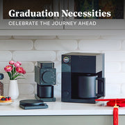 Fellow Ode Brewer next to a Fellow Aiden Coffee maker, scale, red graduation cap and flowers on a white kitchen counter in front of a tiled backsplash. Promotional text overlayed that reads "Graduation Necessities - Celebrate the journey ahead".