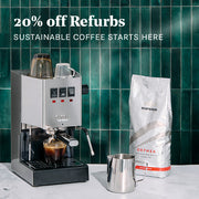 Gaggia Classic Pro in Stainless Steel next to a milk pitcher, bag of Maromas Orphea coffee on a white counter in front of a green tiled wall. Promotional text overlayed that reads "20% Off Refurbs - Sustainable coffee starts here".