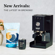 Black Gaggia Classic UP coffee machine with a bag of Crema Wave coffee and a mug on a light surface.