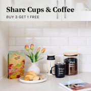 Whole Latte Love Colombia Tolima on a counter next to cups and coffee canisters. Promotional text overlayed that reads "Share Cups & Coffee - Buy 3 Get 1 Free".