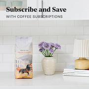 Whole Latte Love Italian Stallion on a white counter top next to flowers in front of a white tiled backsplash. Promotional text that reads "Subscribe and Save with Coffee Subscriptions".