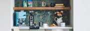 Kitchen setup with Profitec GO Espresso Machine in blue, Eureka grinder, cups, tamper, coffee bags on a shelf and decorative elements in a coffee nook.