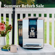 Silver JURA Z6 Super-Automatic espresso machine on an outside table next to grapes, coffee cup and flowers. Promotional text overlayed that reads "Summer Refurb Sale - Certified Refurbished Products".
