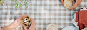 Two people holding coffee cups on a checkered tablecloth.