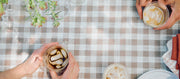Close-up of two people holding coffee cups on a checkered tablecloth.